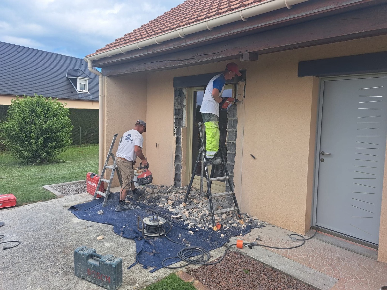 Équipe Dagicour en pleine démolition pour modification d'ouverture sur une façade enduite, gravats et outillage au sol