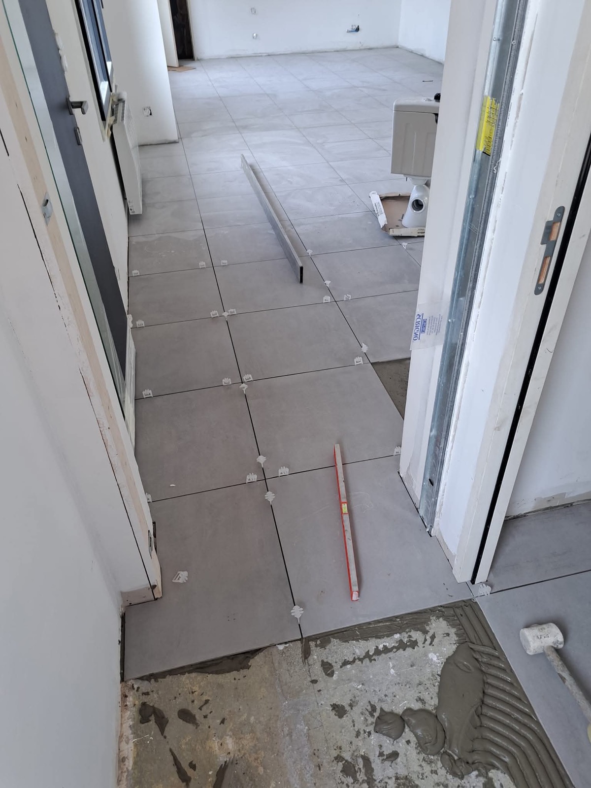 Pose de carrelage grand format grès cérame dans un couloir de maison neuve, croisillons et niveau visibles — Dagicour