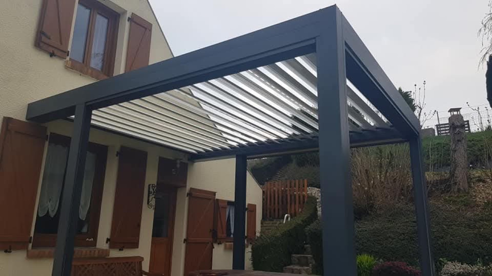 Pergola bioclimatique aluminium à lames orientables ouvertes, posée sur une maison normande — Dagicour