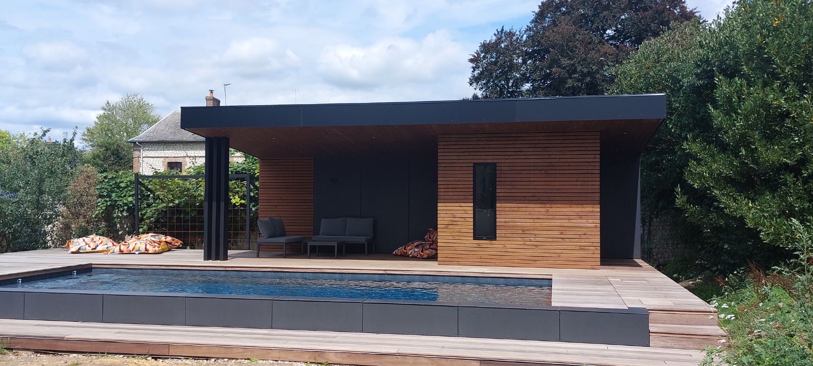 Pool house en bois vu de face avec structure sur pilotis noirs, coussins colorés — Dagicour