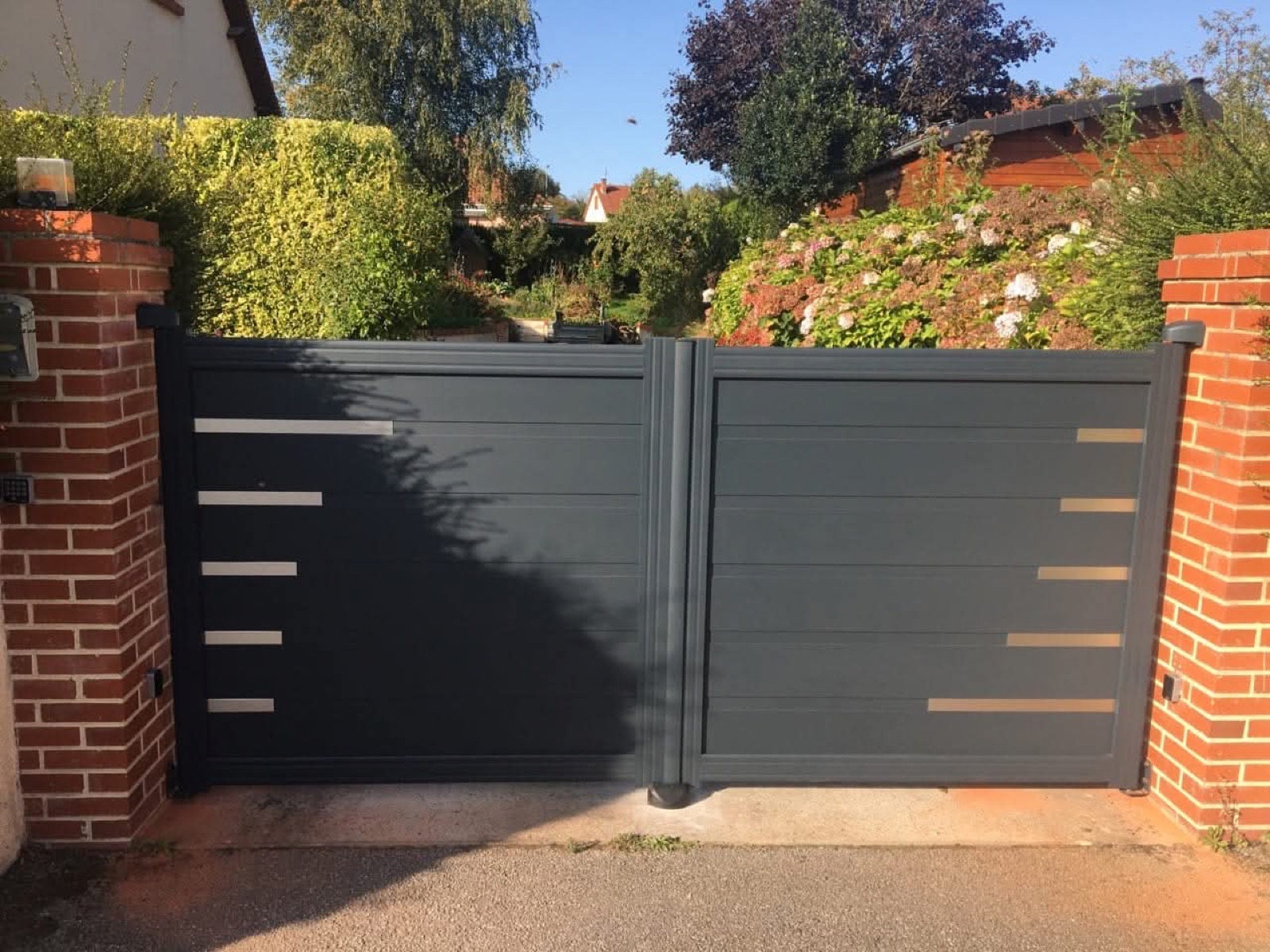 Portail aluminium anthracite double battant avec liserés inox sur piliers briques — réalisation Dagicour en Seine-Maritime
