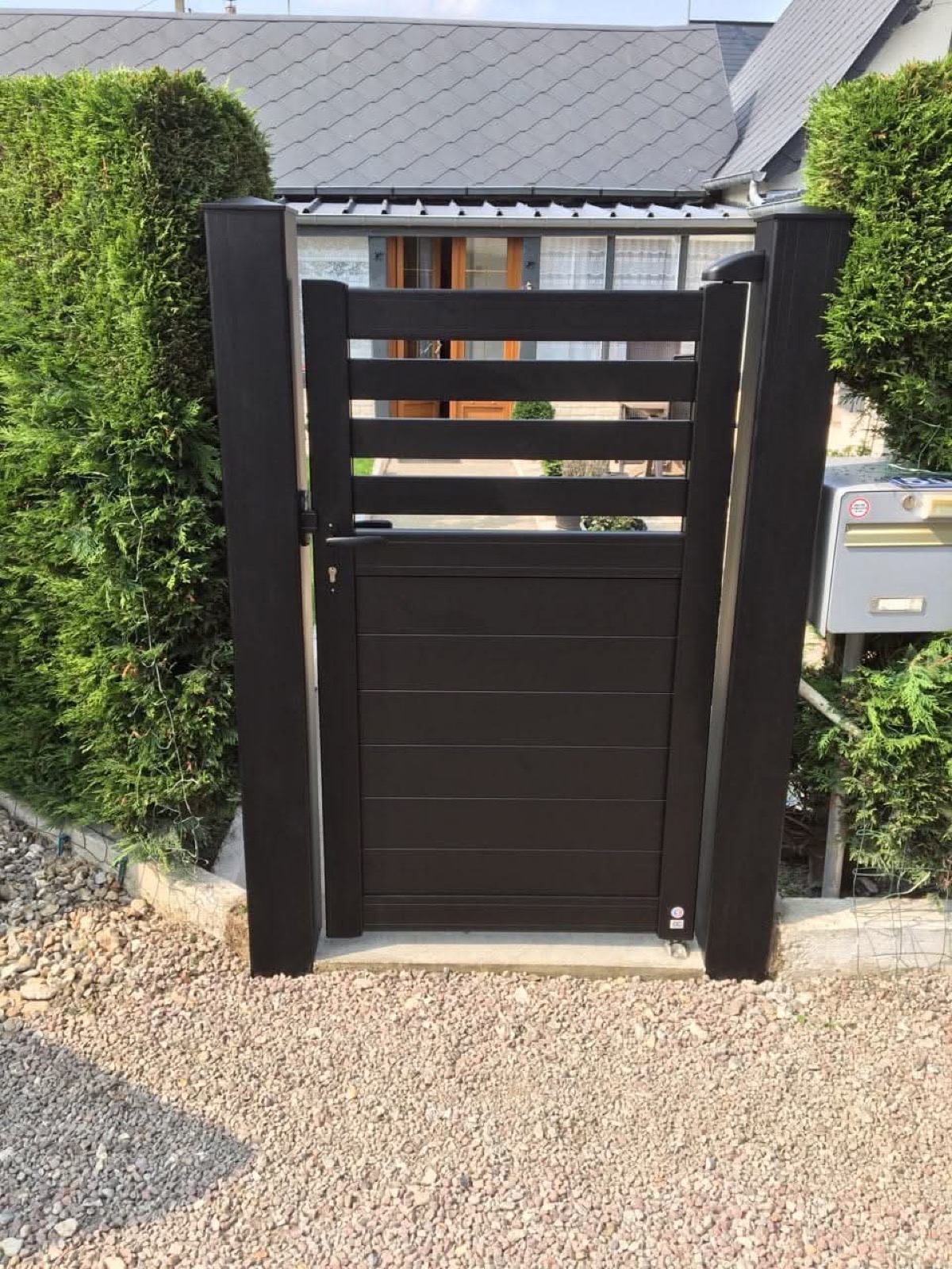 Portillon aluminium anthracite entre deux haies de thuyas — réalisation Dagicour en Normandie