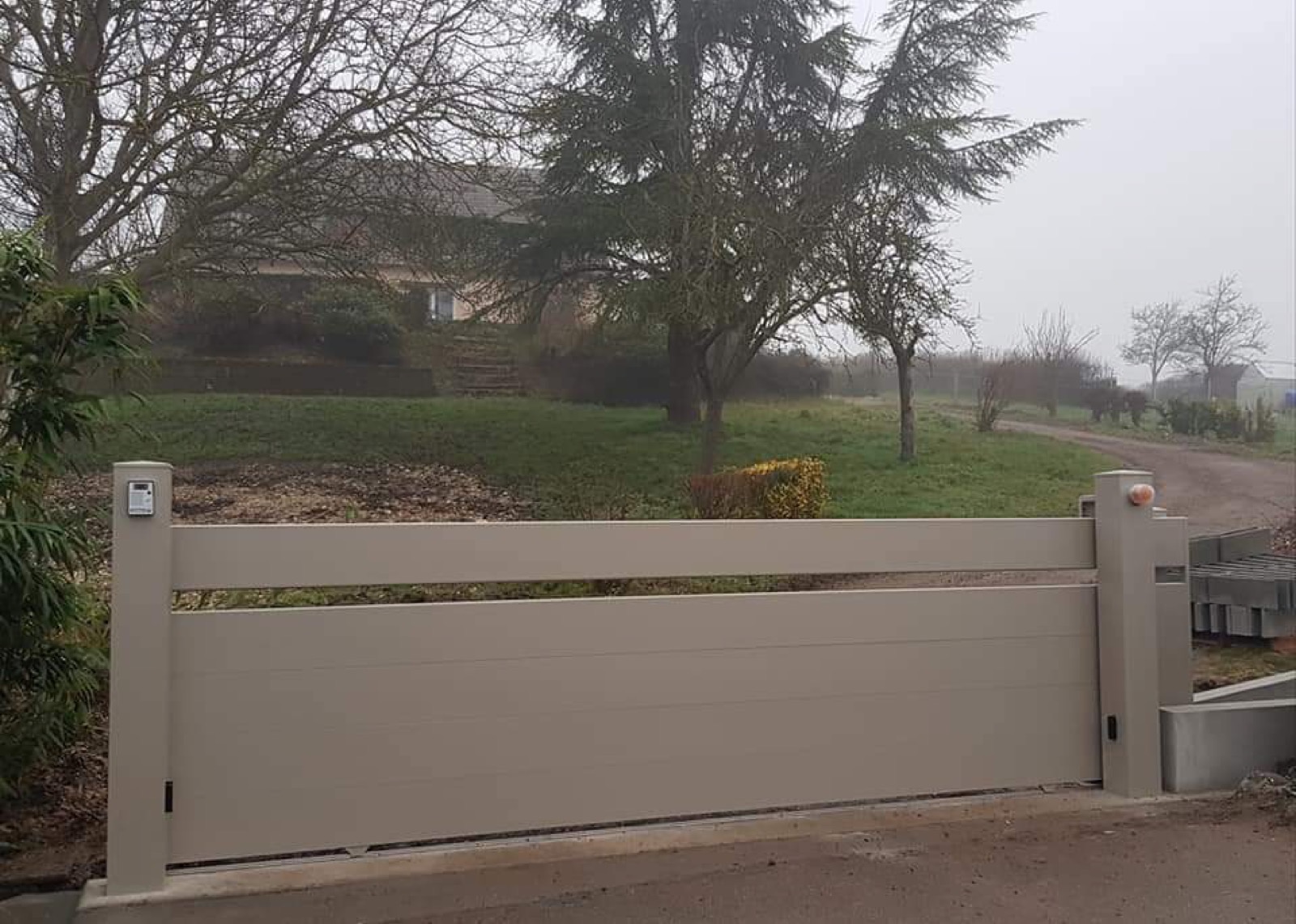 Portail aluminium coulissant taupe, vue depuis l'allée d'une propriété rurale en Seine-Maritime — Dagicour