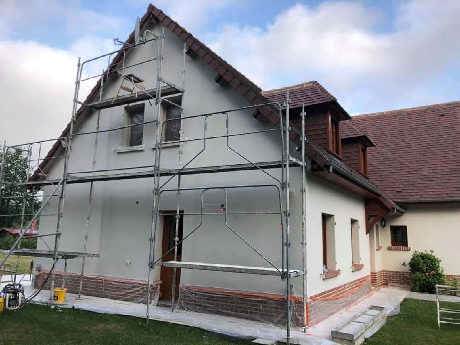 Ravalement de façade en cours, échafaudage et film de protection sur les huisseries, maison normande